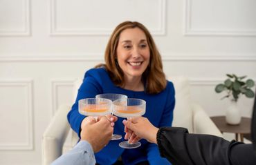 A woman in blue toasts with two others, smiling warmly.