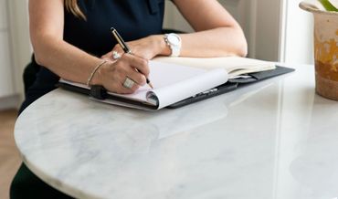 Person writing notes on a clipboard at a marble table.