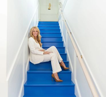 Woman in white suit sitting on bright blue stairs in a narrow hallway.