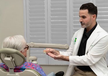 Dentist explaining dental model to elderly patient in clinic.