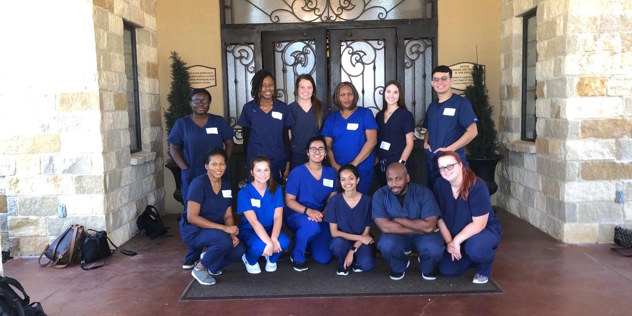 Group of healthcare workers in navy blue scrubs posing outside a building.