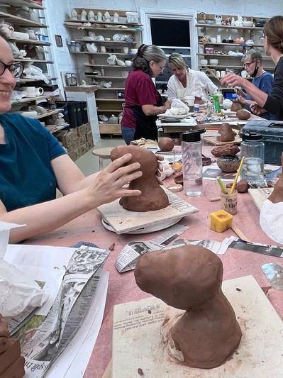 People sculpting clay heads in a pottery class.