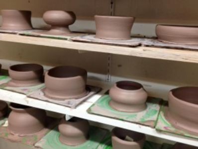 Clay pottery made by students sits to dry on shelves in Artyard Studio.