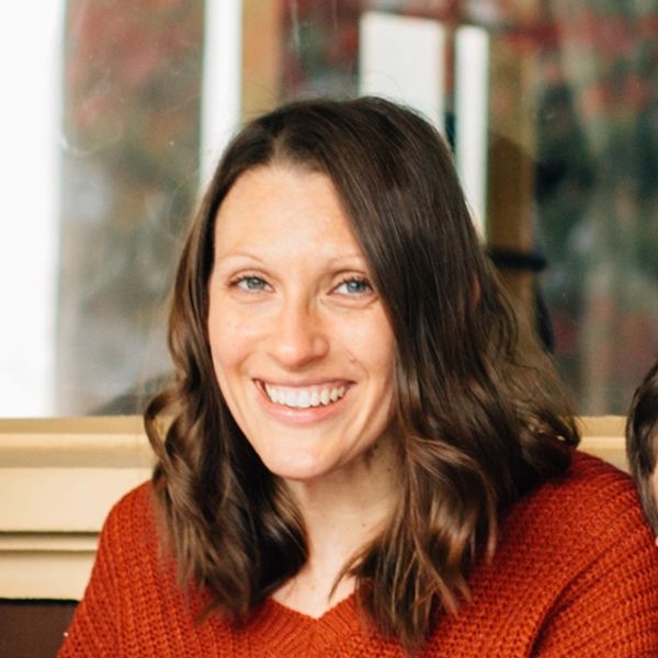 Smiling woman with wavy brown hair wearing a rust-colored sweater.