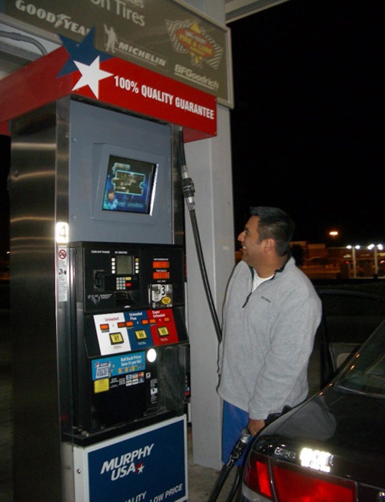 Man fueling car at gas station with TV screen displaying advertisements, highlighting gas pump TV advertising effectiveness for targeted marketing.
