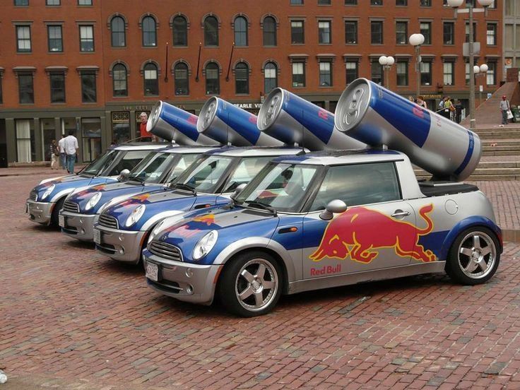 Red Bull-branded Mini Cooper cars with large cans mounted on top, showcasing creative guerrilla marketing strategy in an urban setting.