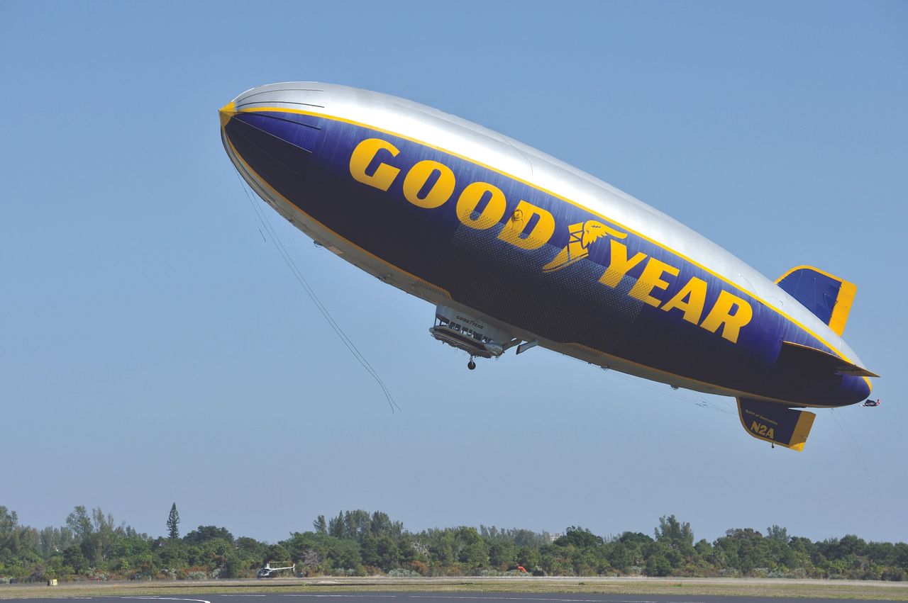 Goodyear blimp flying over landscape, showcasing aerial advertising in action for marketing strategies.