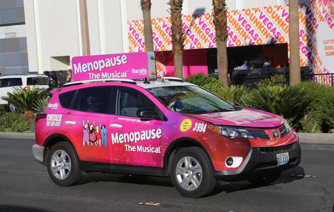 Rideshare vehicle advertising "Menopause The Musical" with vibrant pink branding, showcasing promotional content for Las Vegas entertainment.