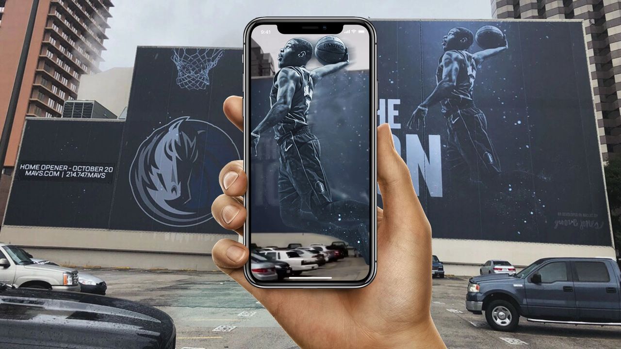 Virtual reality (VR) and augmented reality (AR) are revolutionary Hand holding smartphone displaying augmented reality basketball player over large outdoor billboard promoting home opener, highlighting innovative AR applications in outdoor advertising.