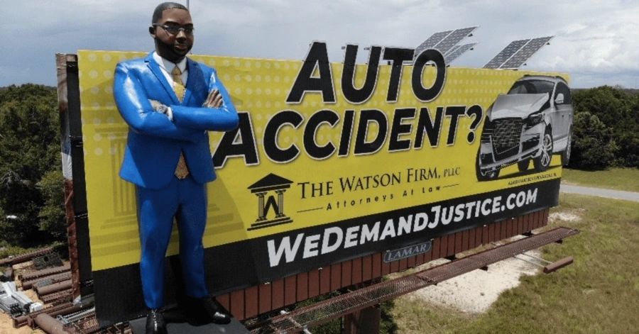 Billboard advertisement featuring a life-sized figure of a lawyer in a blue suit, promoting the Watson Firm with the text "AUTO ACCIDENT?" and a graphic of a car, emphasizing legal services for accident victims.