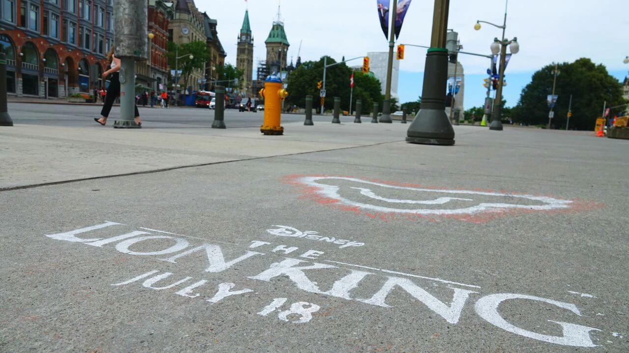 Evolving beyond traditional marketing, daring brands are taking to the pavements with innovative sidewalk stencil designs that turn heads and create buzz. Sidewalk stencil advertisement for Disney's "The Lion King," featuring bold typography and date "July 18," integrated into an urban setting with pedestrians and city landmarks in the background.