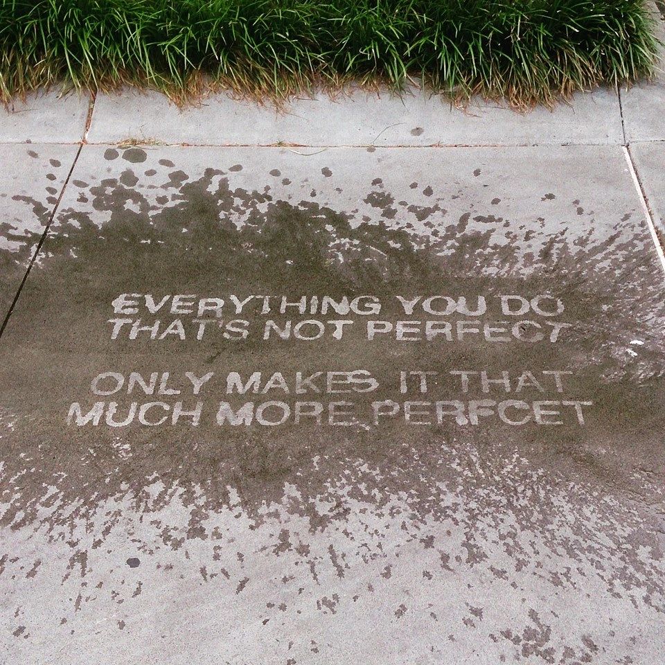 Water stencil artwork on sidewalk featuring motivational text: "Everything you do that's not perfect only makes it that much more perfect," surrounded by splashes of water.