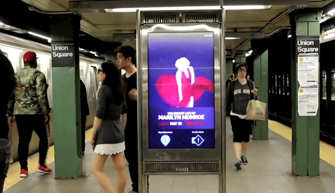 Subway advertising display featuring a vibrant promotional poster for "The Secret Life of Marilyn Monroe" at Union Square station, with commuters walking by in a busy subway environment.