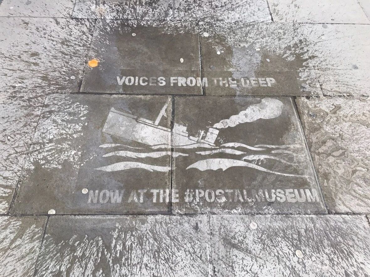 This makes a very noticeable "clean" region that surprises and draws attention Water stencil sidewalk advertisement featuring a ship and the text "Voices from the Deep" and "Now at the #PostalMuseum," illustrating guerrilla marketing techniques.