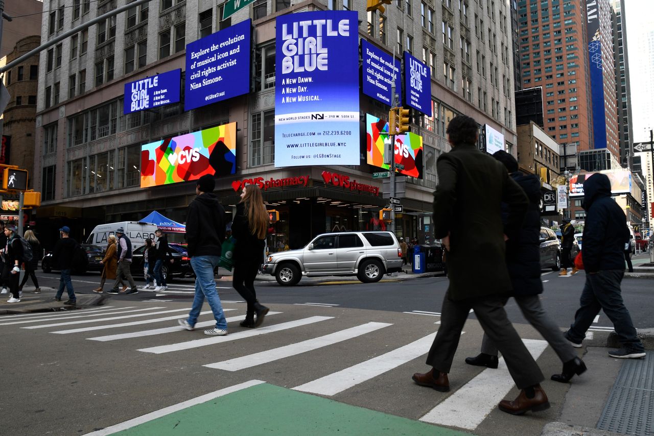 Digital billboards have revolutionized the advertising industry, offering dynamic and visually captivating displays that grab the attention of passersby. Digital billboards displaying "Little Girl Blue" musical advertisement and CVS logo in a busy urban crosswalk with pedestrians.