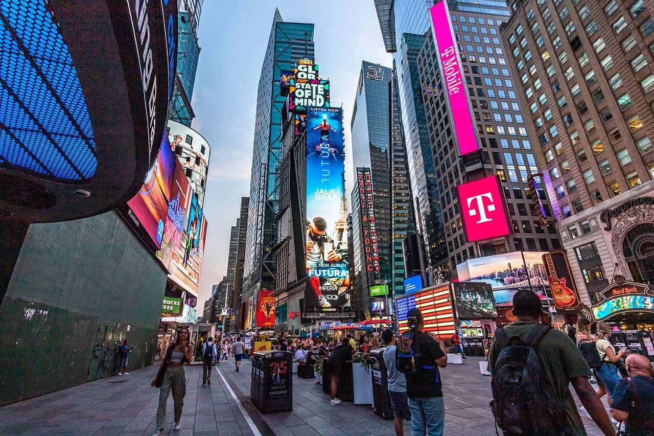 Billboard in Times Square displaying digital advertisements, including music promotions and brand logos, with pedestrians and a vibrant urban setting.