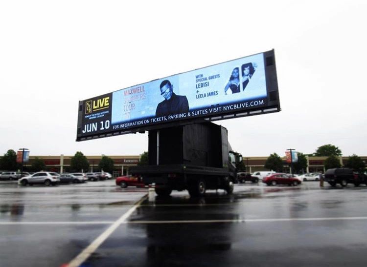Mobile billboard advertising Maxwell's Summer Tour featuring special guests Ledisi and Leela James, displayed in a parking lot setting with a cloudy sky.