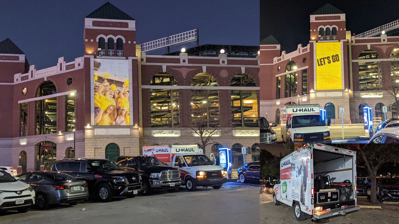U-Haul trucks parked near a stadium, featuring a large digital billboard displaying "LET'S GO" and a crowd cheering, showcasing street advertising potential in urban settings like Atlanta, GA.