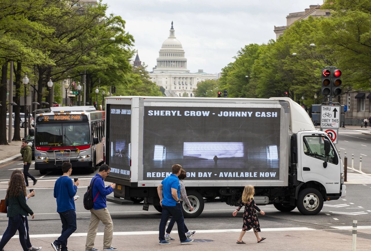 LED billboard truck promoting Sheryl Crow and Johnny Cash's "Redemption Day" during Washington DC protest, with U.S. Capitol in background, pedestrians crossing street.