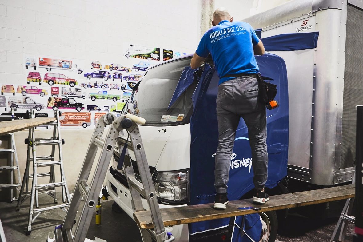 Person applying a Disney-themed vehicle wrap in a workshop, showcasing the car wrapping process for advertising.
