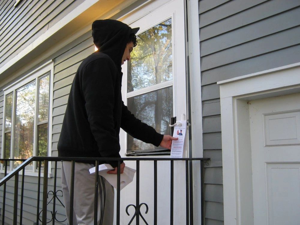 Person distributing a door hanger at a residential entrance, illustrating effective guerrilla marketing strategies for local advertising.