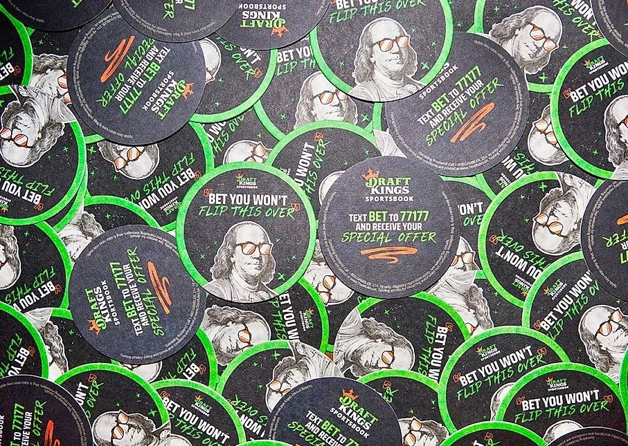 DraftKings promotional coasters featuring Benjamin Franklin illustration, slogans "Bet You Won't Flip This Over" and "Text BET to 71777 for your special offer," surrounded by a vibrant green border, emphasizing guerrilla marketing tactics for brand awareness.
