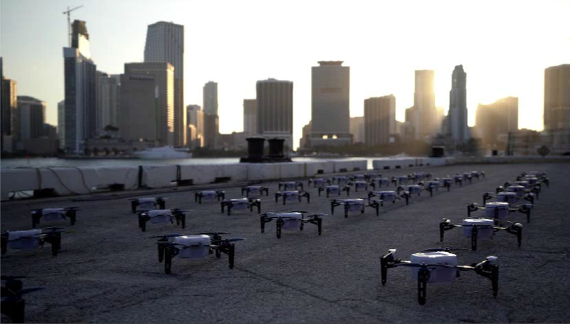 To ensure high-quality footage and seamless execution of your drone-based advertisements, it is advisable to hire a professional drone operator. Rows of drones on a waterfront, with a city skyline in the background, illustrating the setup for a drone light show and emphasizing innovative entertainment technology.