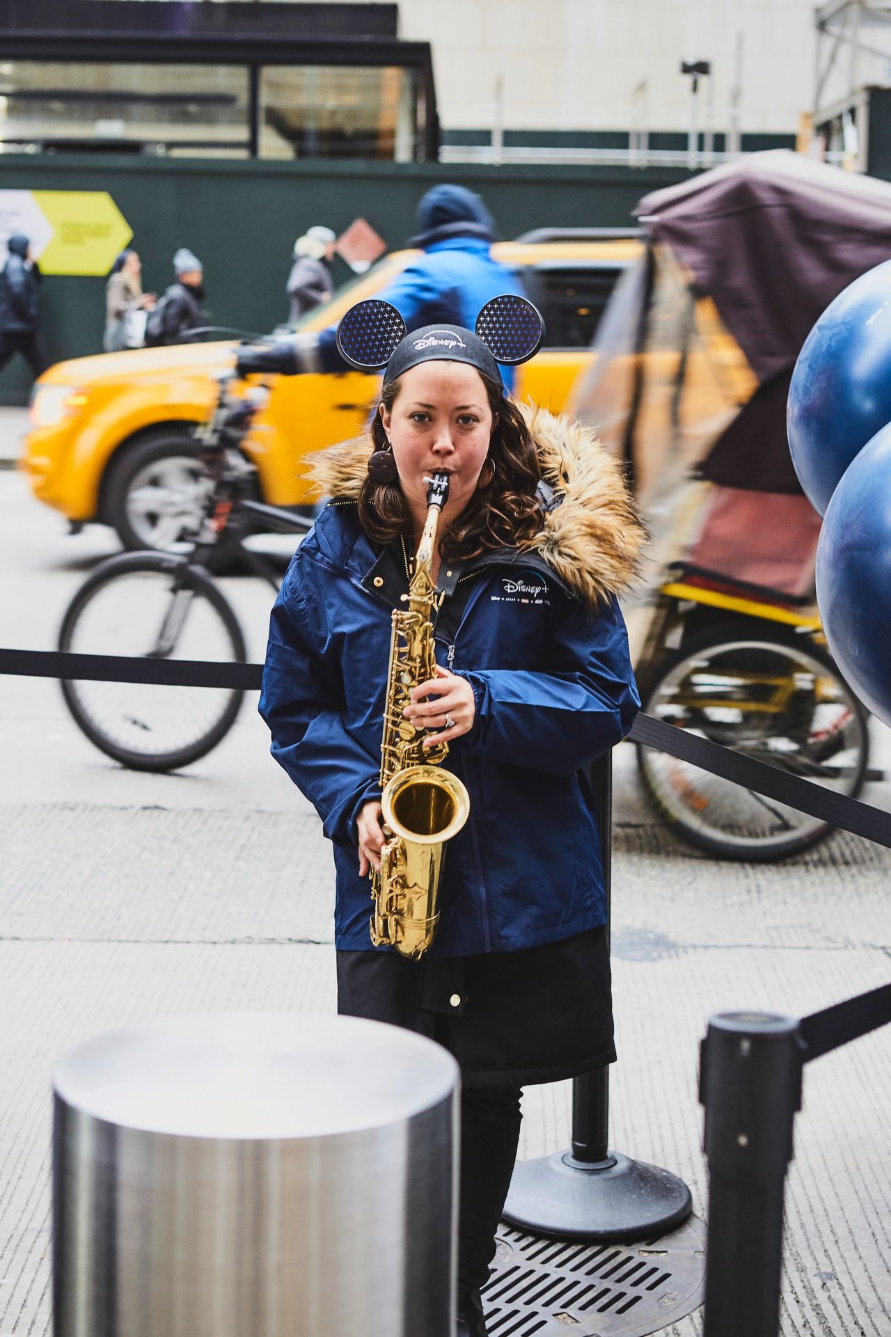 Musician wearing Disney+ ears playing saxophone in urban setting, capturing attention and creating a vibrant atmosphere for guerrilla marketing.