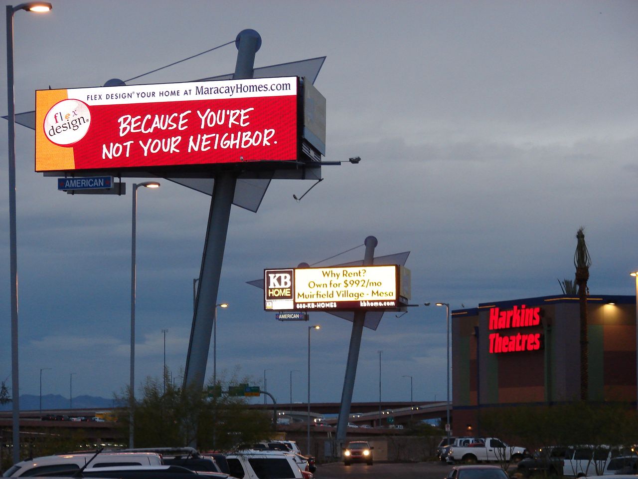 The large size and elevated position of highway billboards enhance their visibility from afar. Highway billboard advertising showcasing "Flex Design" with tagline "Because you're not your neighbor" and additional KB Home advertisement, emphasizing impactful out-of-home marketing strategies.