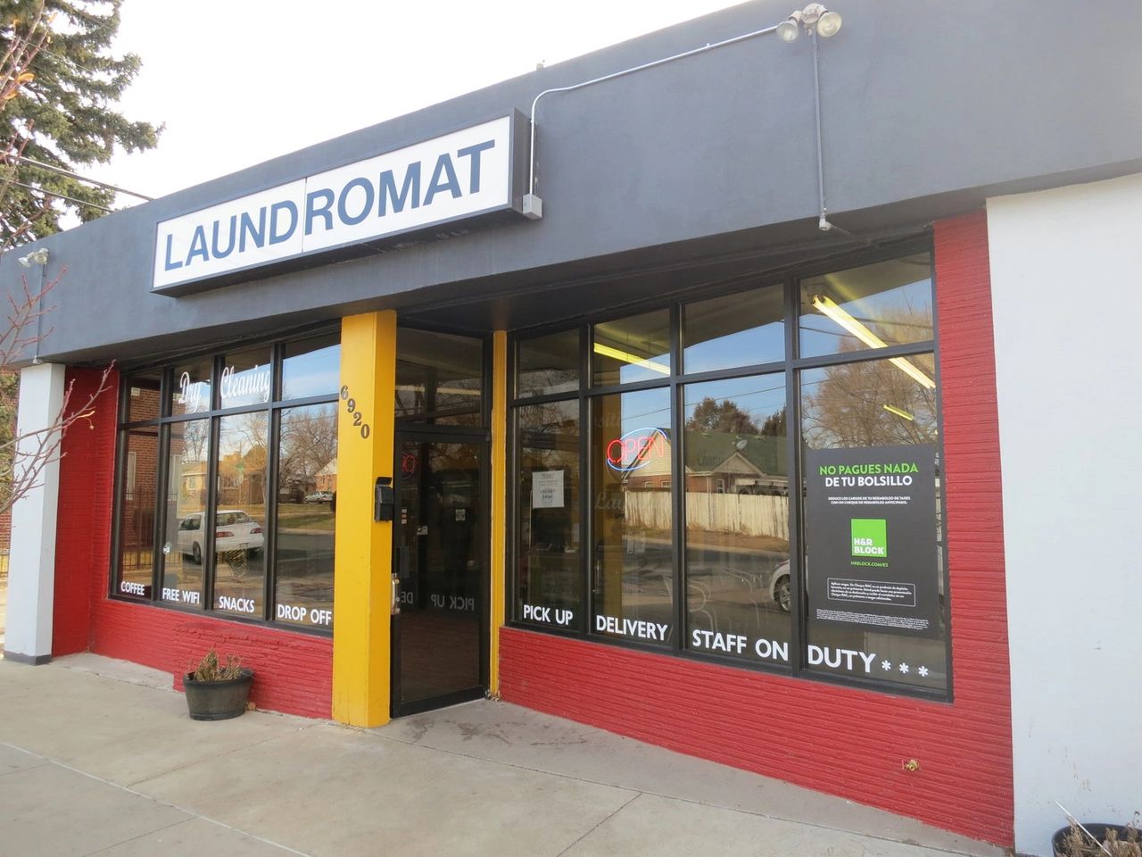 Laundromat exterior with signage displaying "LAUNDROMAT," "Dry Cleaning," and services like "Coffee," "Free WiFi," and "Snacks," emphasizing customer convenience and local business visibility.