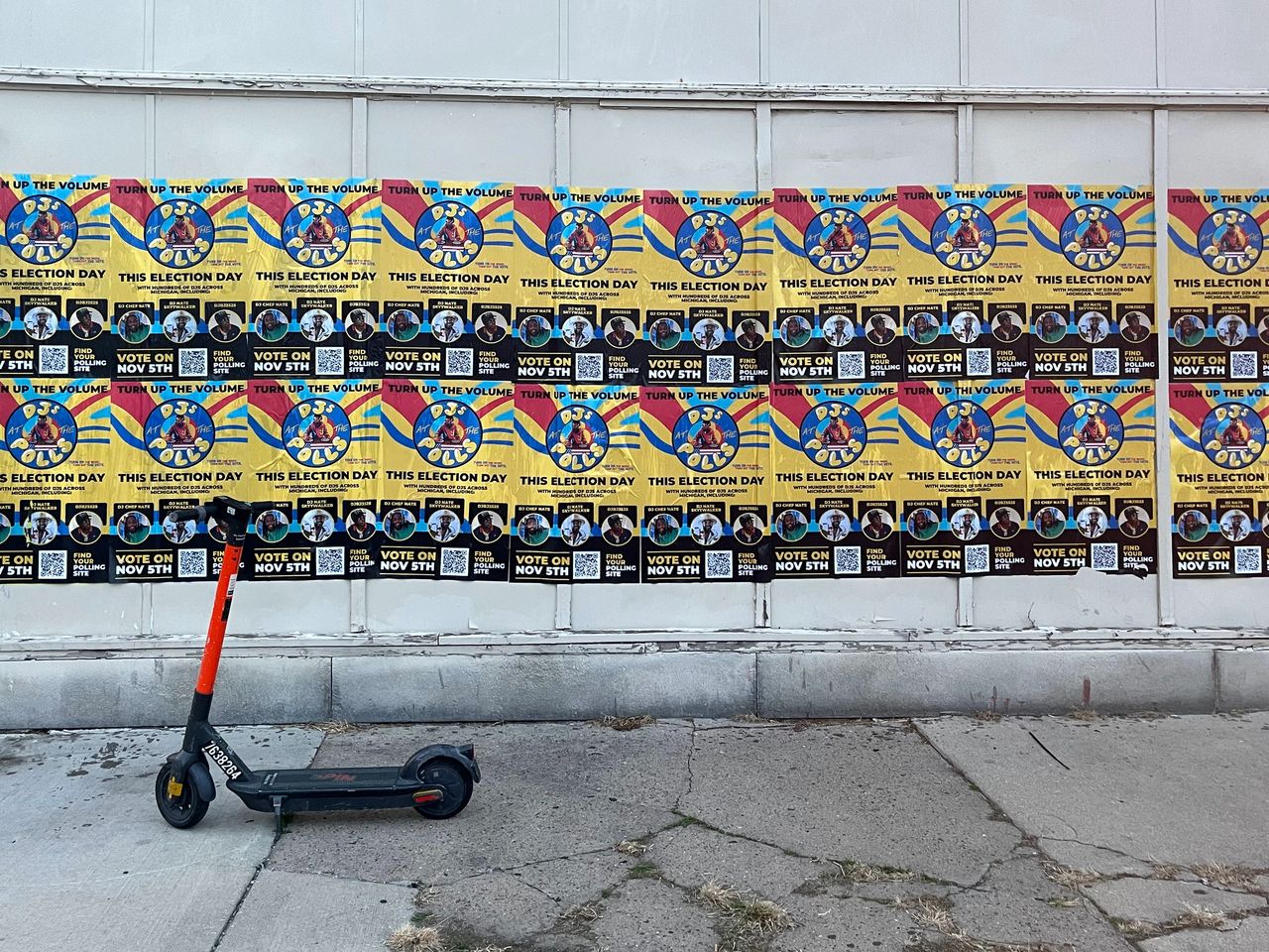 Colorful election posters promoting voting on November 5th, featuring the phrase "Turn Up the Volume" and vibrant graphics, displayed on a wall with a scooter parked in front.