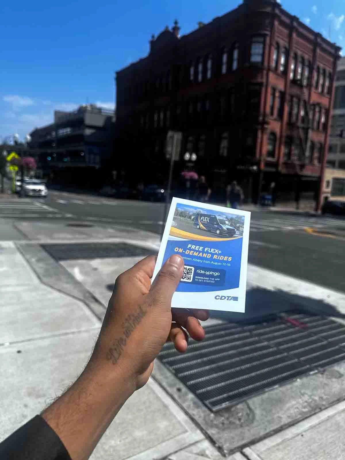 Hand holding promotional flyer for free on-demand rides in urban setting, featuring a blue and white design with QR code, street advertising in Washington, D.C.