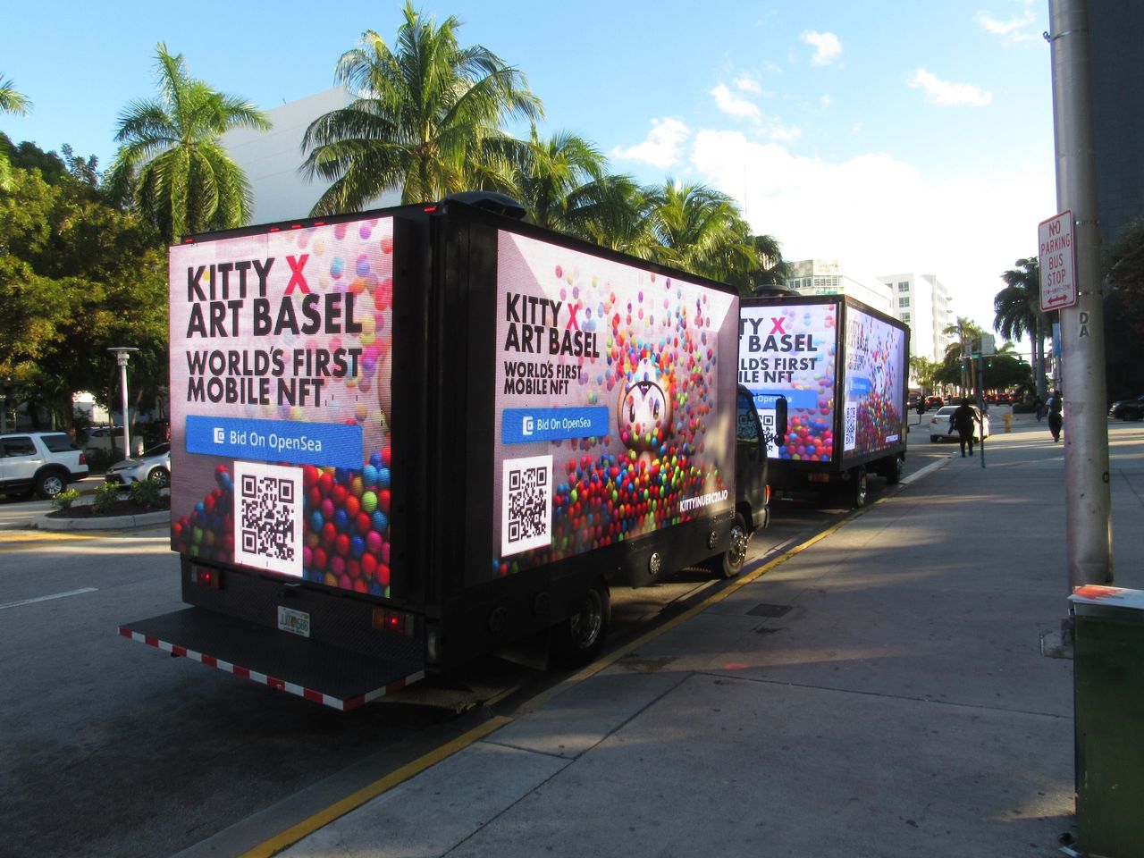 LED billboard trucks displaying "KITTY X ART BASEL" and "WORLD'S FIRST MOBILE NFT" in vibrant colors, promoting mobile advertising in Miami.