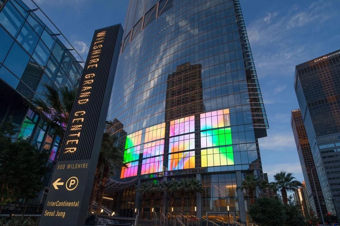 Illuminated digital billboard on the Grand Center building in Los Angeles, showcasing vibrant colors and reflections, surrounded by palm trees and urban architecture, highlighting prime advertising space.