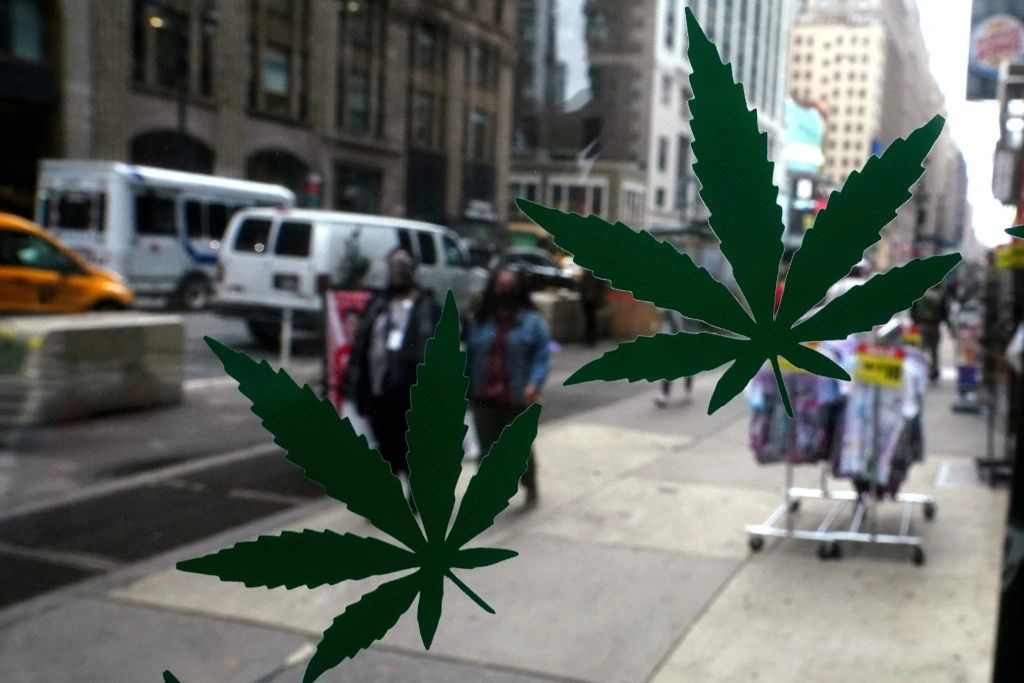 Green cannabis leaves on a storefront window, with a bustling New York City street scene in the background, reflecting the cannabis industry's visibility and compliance focus.