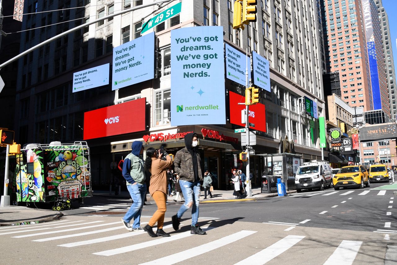Billboard advertisements for NerdWallet displaying "You've got dreams. We've got money, Nerds." in a busy urban setting with pedestrians crossing at a street intersection near CVS.