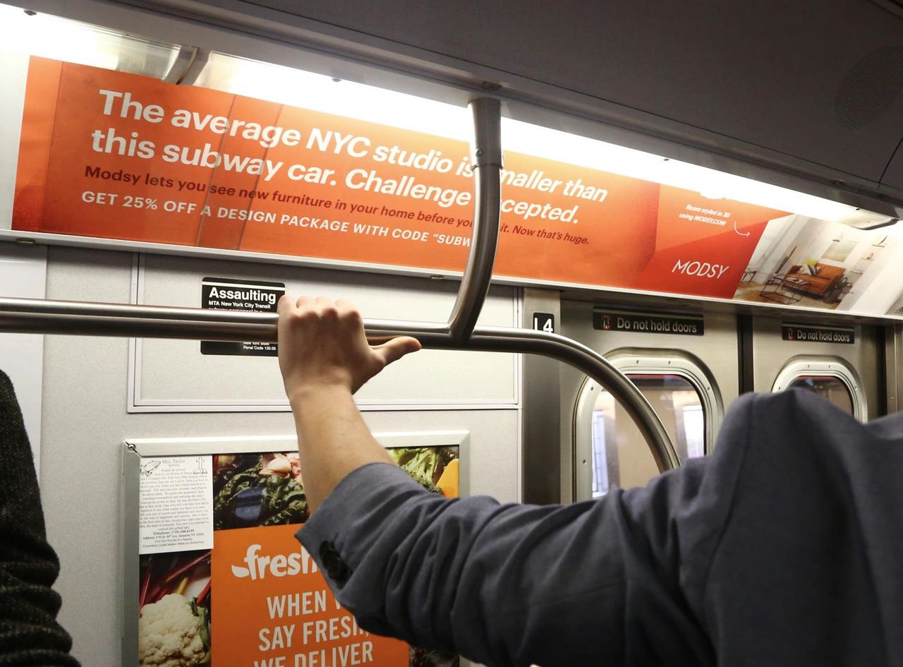 Subway interior featuring an advertisement for Modsy, promoting interior design services with a focus on small NYC apartments, highlighting a discount offer.
