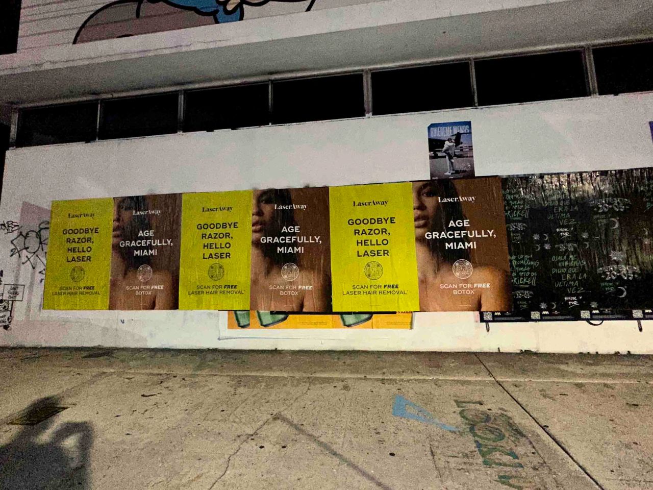 Posters advertising LaserAway's services, featuring phrases "Goodbye Razor, Hello Laser" and "Age Gracefully, Miami," promoting laser hair removal and Botox, set against a graffiti-covered wall in an urban environment.
