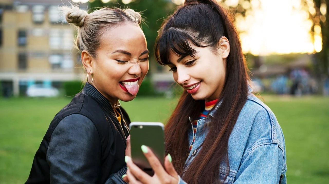 Two young women engaging with a smartphone, showcasing digital interaction and social connection, reflecting millennial consumer behavior and marketing strategies.