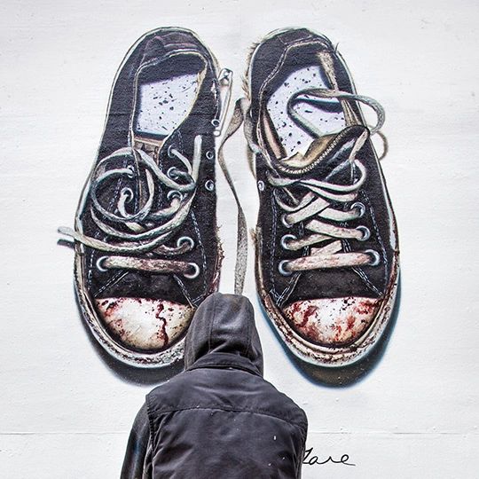Mural of oversized, worn black sneakers with visible wear and stains, person in a hoodie interacting with the artwork, symbolizing community engagement and emotional connection in marketing strategies.