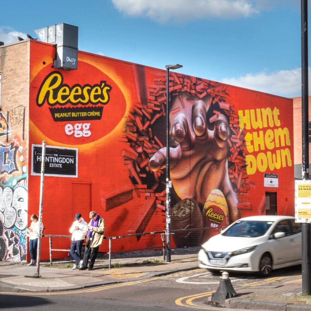 Mural featuring Reese's Peanut Butter Cr&egrave;me egg with a prominent hand reaching out and the text "Hunt them Down," symbolizing creative advertising in urban settings, reflecting innovative marketing strategies.