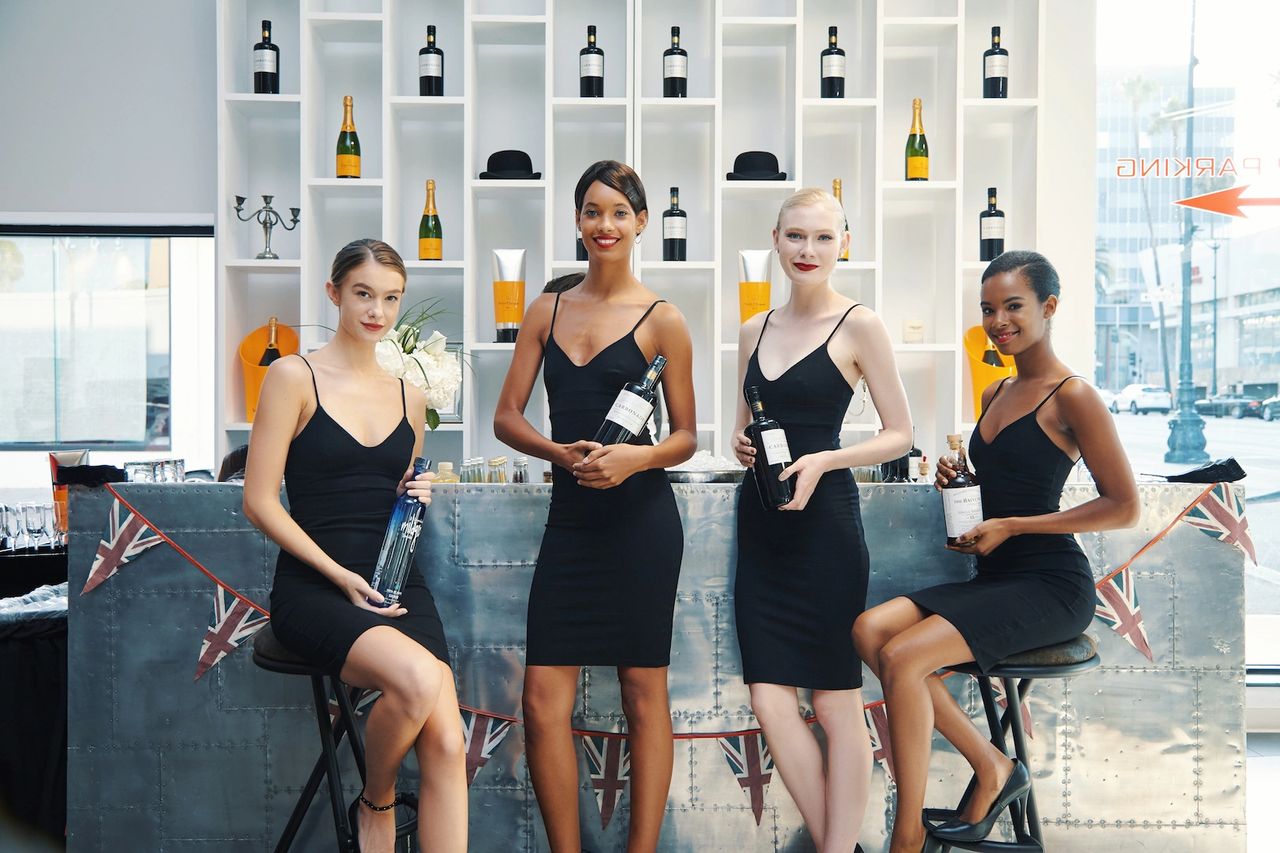 Four professional brand ambassadors in black dresses, showcasing beverages at a stylish event bar, enhancing brand engagement and atmosphere.