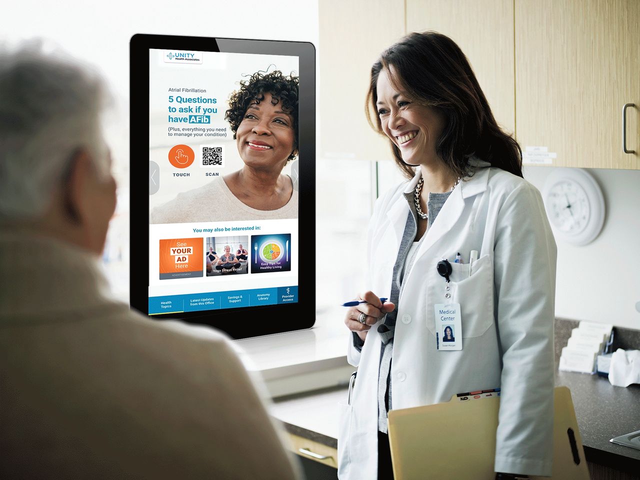 Doctor interacting with patient in a healthcare setting, digital tablet displaying health information about Atrial Fibrillation, emphasizing patient engagement and digital advertising in healthcare.