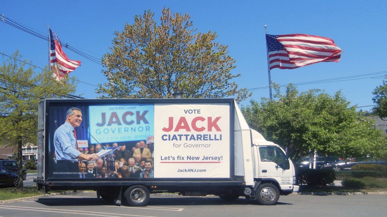 Political advertisement truck featuring Jack Ciattarelli for Governor, with campaign slogan "Let's fix New Jersey!" and American flags in the background.
