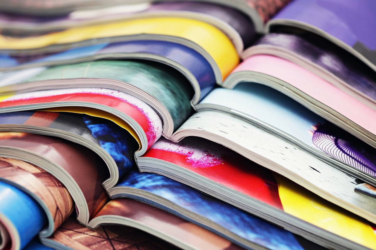 Colorful stacked magazines showcasing vibrant print advertising designs, emphasizing the effectiveness of print media in marketing strategies.