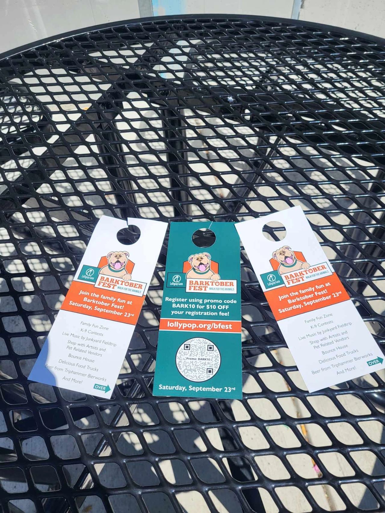 Door hangers promoting Barktober Fest event with details about family activities, live music, and registration discount, displayed on a black metal table.