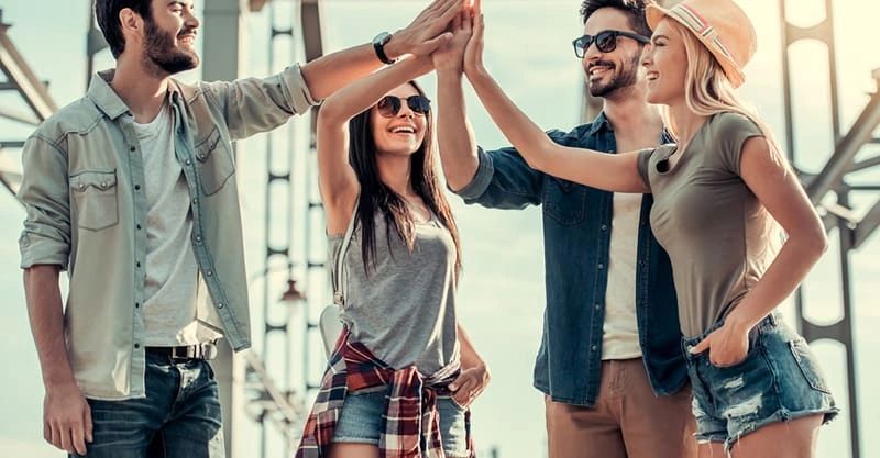 Group of four diverse young adults celebrating with high-fives outdoors, embodying teamwork and community engagement in guerrilla marketing strategies.