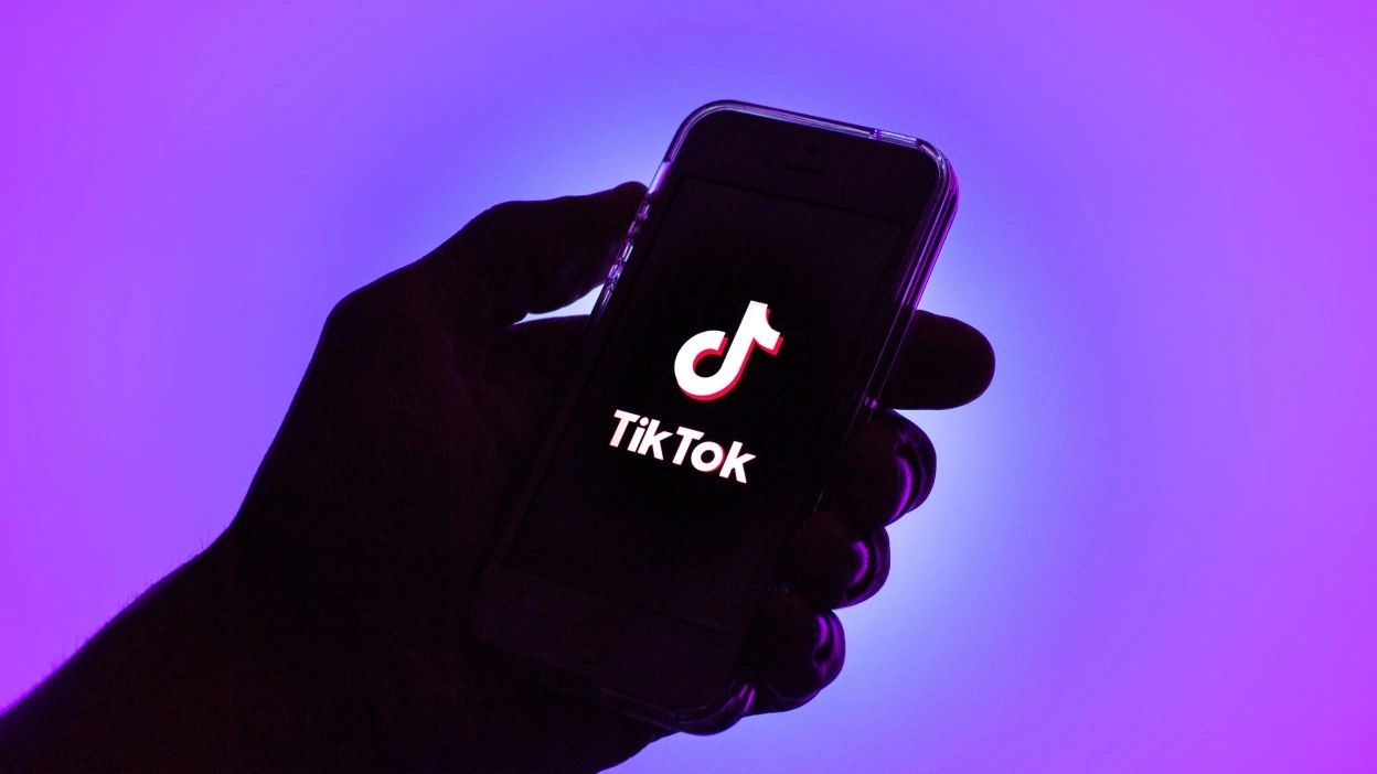 Hand holding smartphone displaying TikTok logo against a vibrant purple background, emphasizing TikTok's role in cost-effective marketing for small businesses.