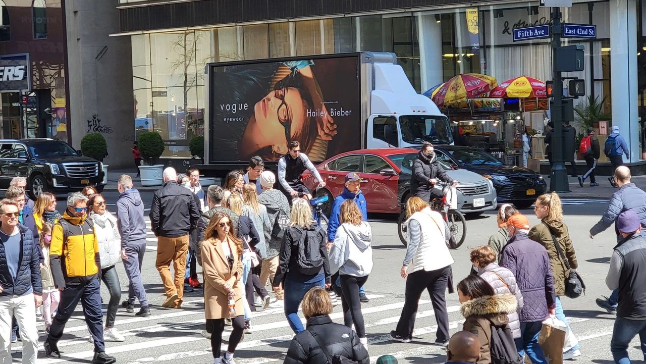 Crowd of pedestrians crossing a busy street with a Vogue Eyewear advertisement featuring Hailey Bieber in the background, highlighting guerrilla marketing's impact on consumer engagement.