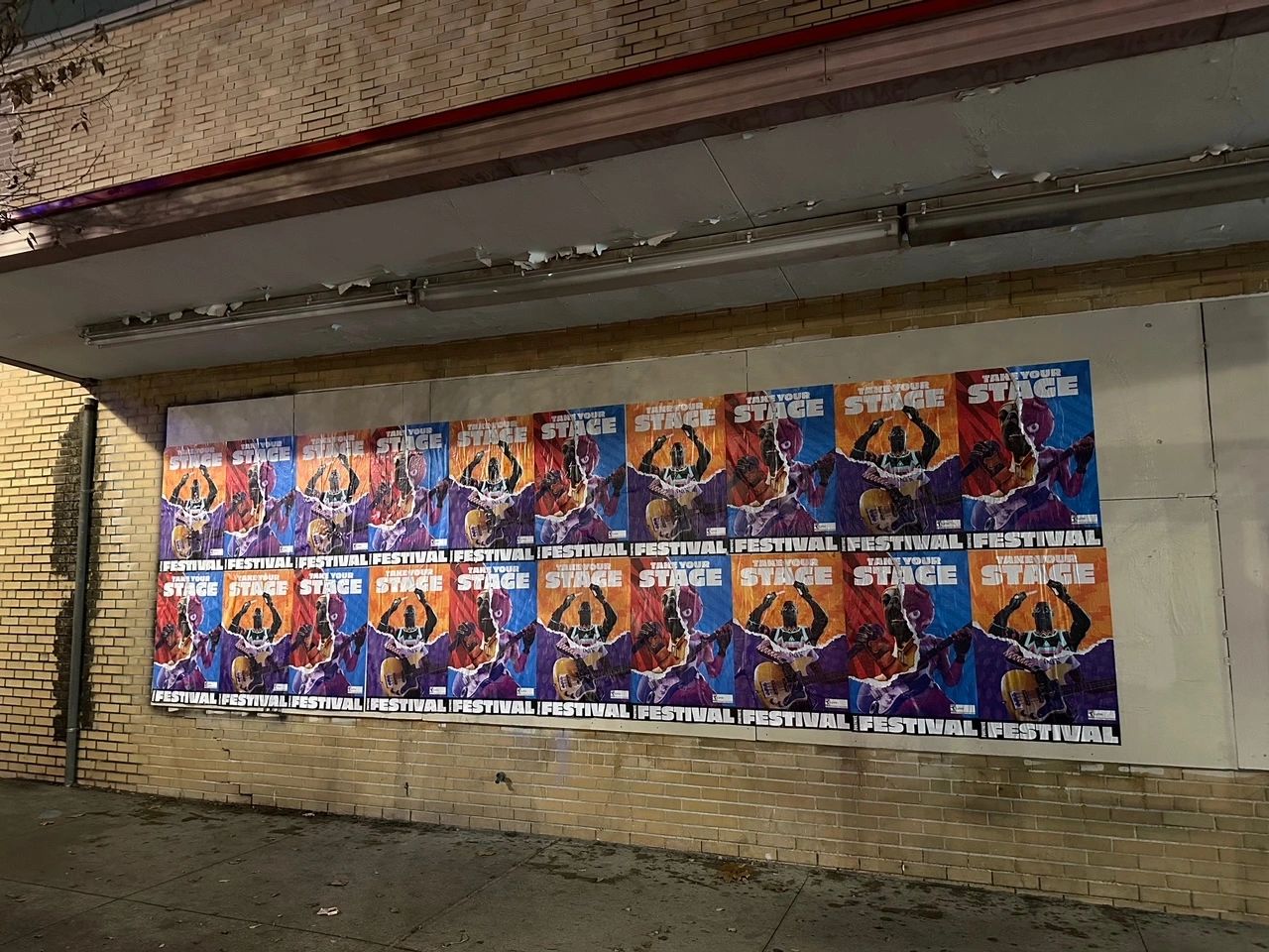 Colorful festival posters promoting "Take Your Stage" displayed on a brick wall, highlighting vibrant graphics and engaging designs relevant to poster marketing strategies in West Virginia.